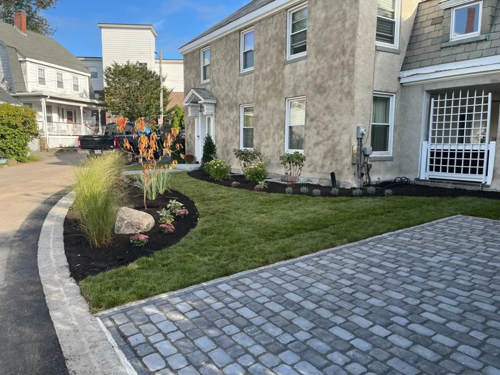 The completed landscape renovation in Lynn, MA, by Leahy Landscaping, featuring a new paver patio, lush sod lawn, and mulched garden bed.